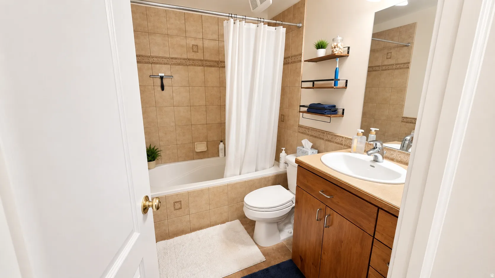 Bathroom featuring a built-in bathtub with shower, tiled surround, wood-finish vanity with an integrated sink, and an overhead lighting fixture