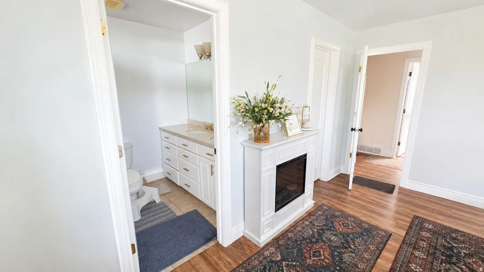 Room featuring wood-finish flooring, a decorative white fireplace with an electric insert, and light-colored wall paint