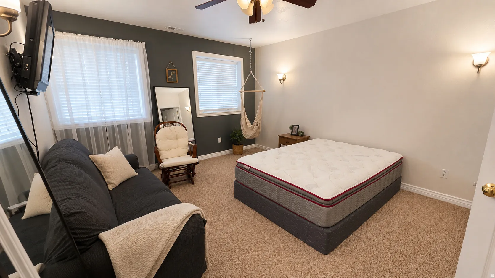 Carpeted room featuring dual wall sconces, two windows with white blinds, and a ceiling fan with integrated lighting