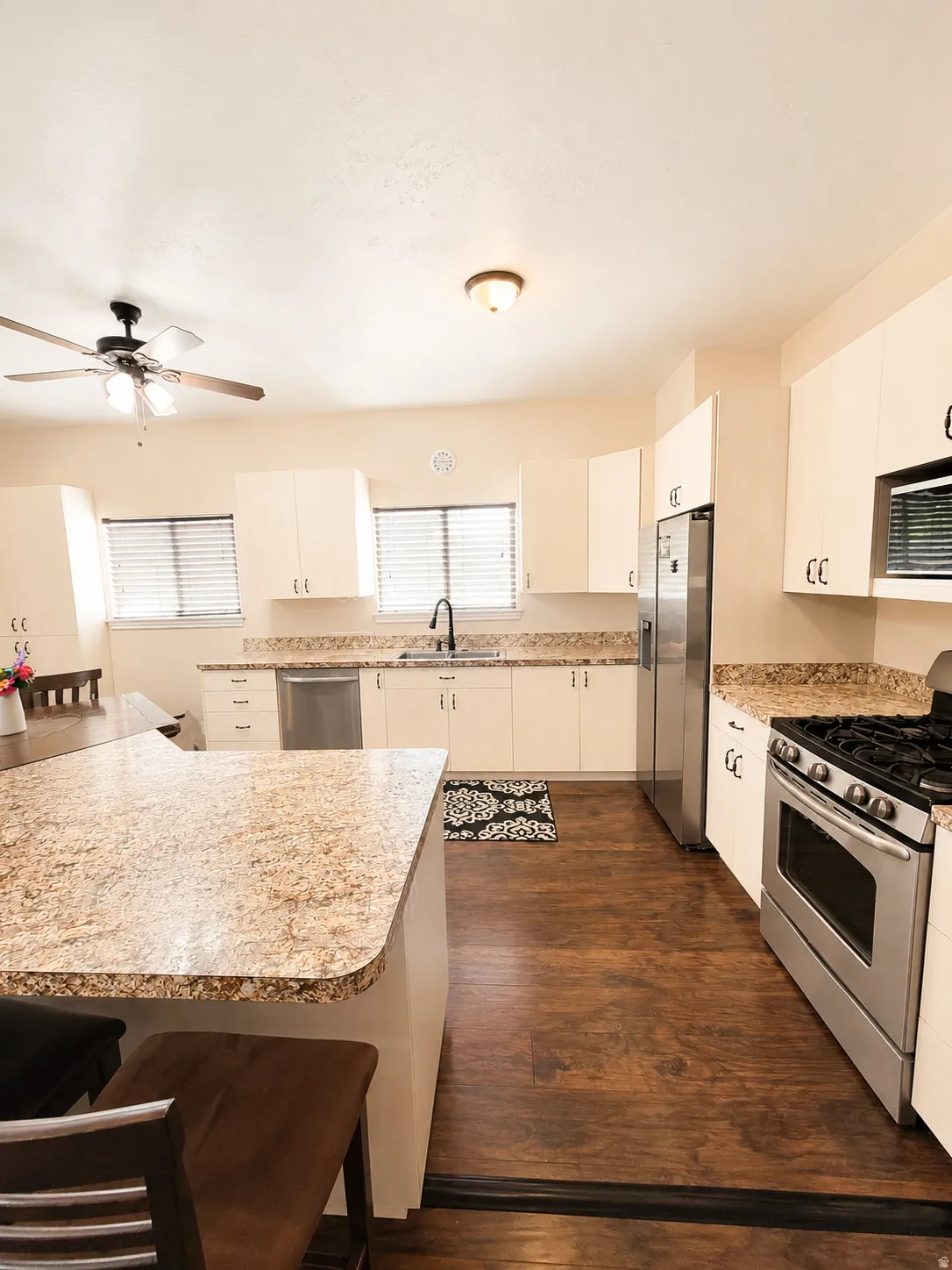 ADU #2 - Kitchen featuring an eat-at island with speckled countertops, white cabinetry, dark wood-finish flooring, and stainless steel appliances