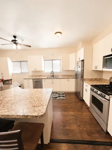ADU #2 - Kitchen featuring an eat-at island with speckled countertops, white cabinetry, dark wood-finish flooring, and stainless steel appliances