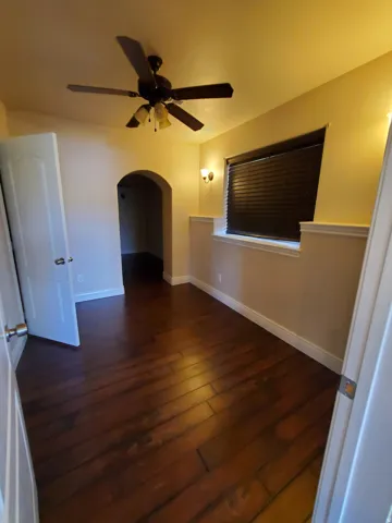 Room featuring wood-finish flooring, a ceiling fan with integrated lighting, and a window with horizontal blinds