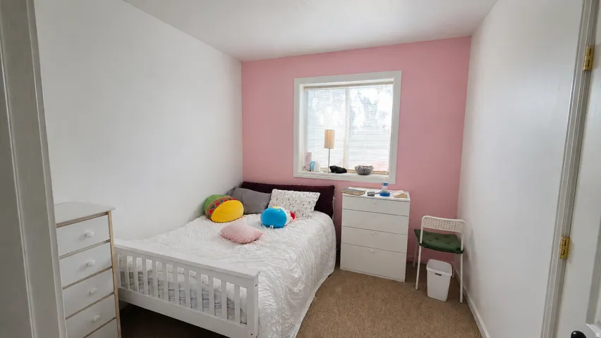 Bedroom featuring a window with white trim, a pink accent wall, and neutral carpeting