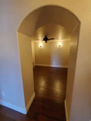 Arched entryway revealing a room with wood-finish flooring, a ceiling fan, and two wall-mounted sconces