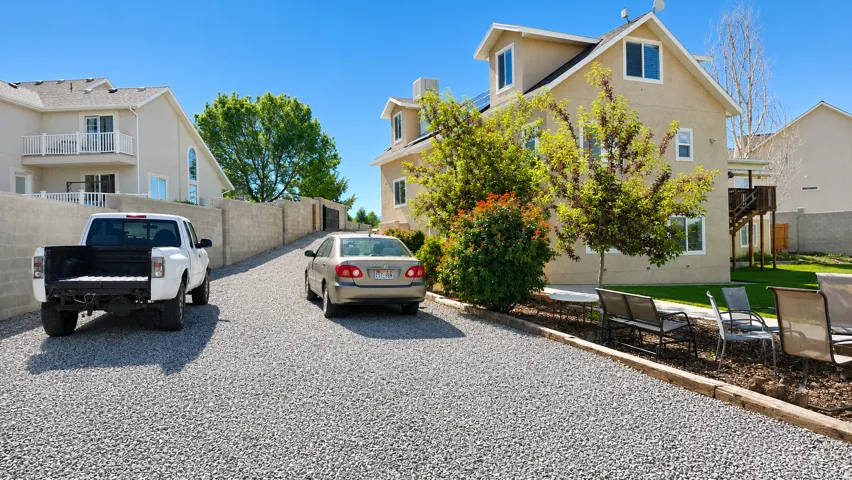 Spacious gravel driveway providing ample parking, bordered by a concrete block privacy wall and established landscaping