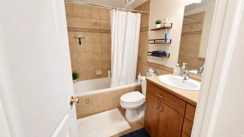 Bathroom featuring a built-in bathtub with shower, tiled surround, wood-finish vanity with an integrated sink, and an overhead lighting fixture
