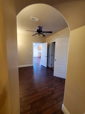 Archway entry into a room featuring wood-finish flooring, a ceiling fan with integrated lighting, and light-toned wall paint