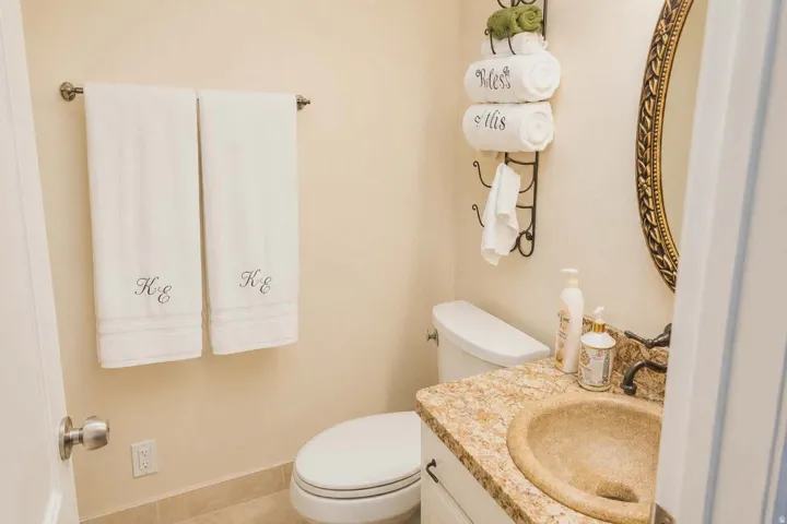 Powder room featuring a stone countertop vanity with a bronze-finish faucet, an oval mirror with an ornate frame, ceramic tile flooring, and a towel bar