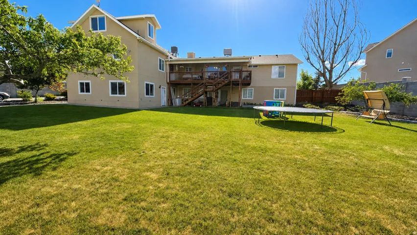 Expansive rear yard featuring a manicured lawn, multi-level deck with wood railing, and mature landscaping