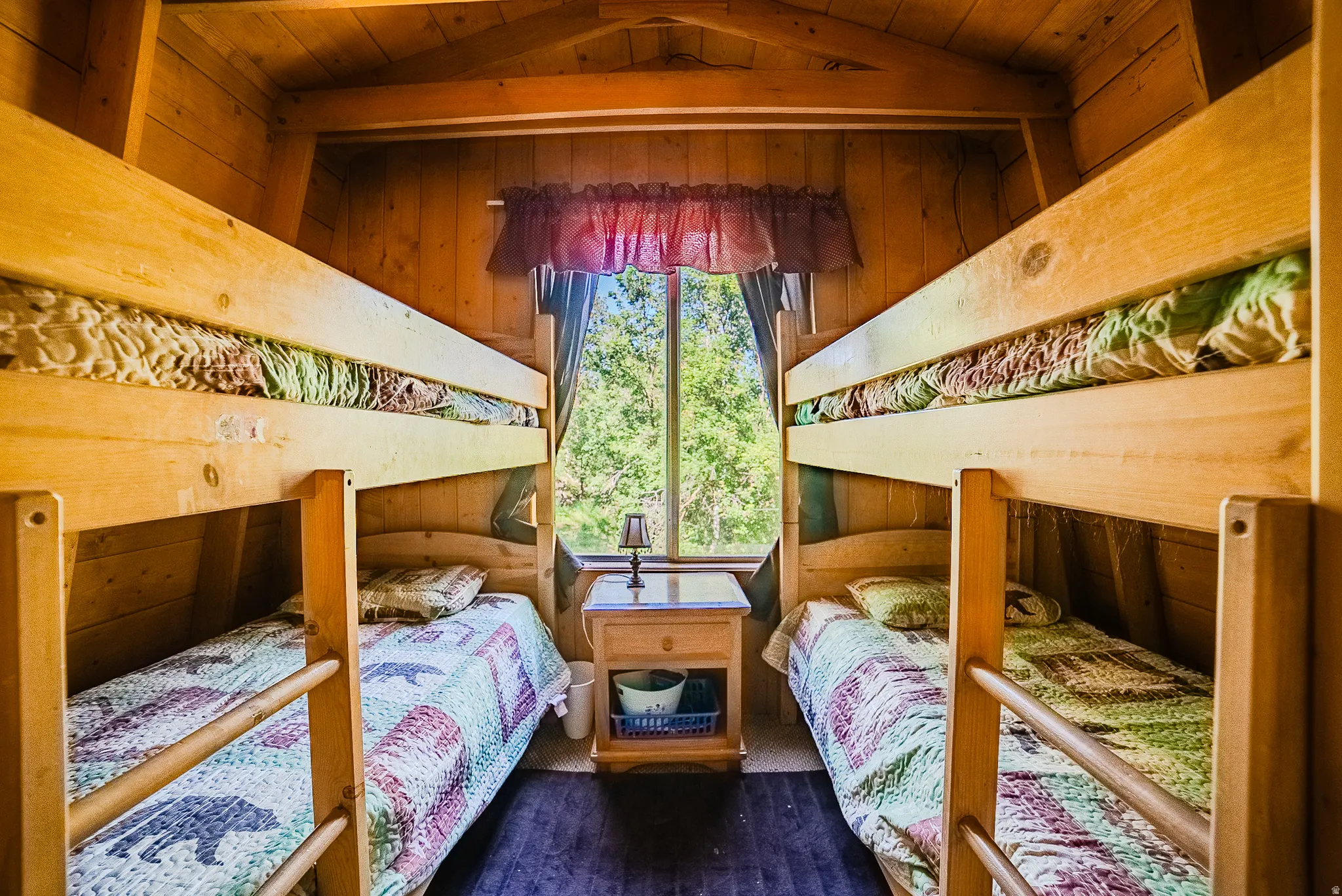 Wood-paneled room featuring two bunk beds with natural wood frames, dark flooring, and a central window