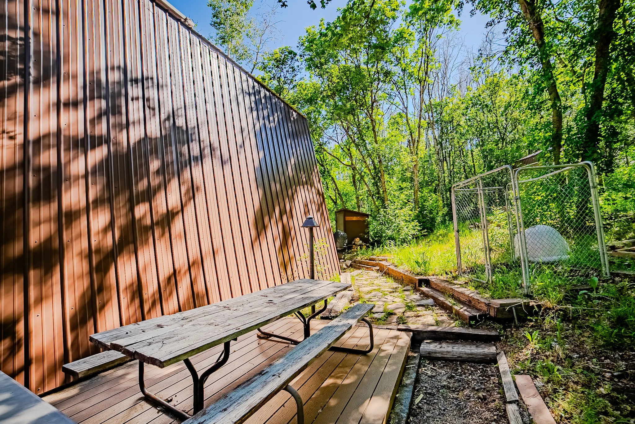 Wood-finish deck with a built-in picnic table, corrugated metal siding, and surrounded by mature trees