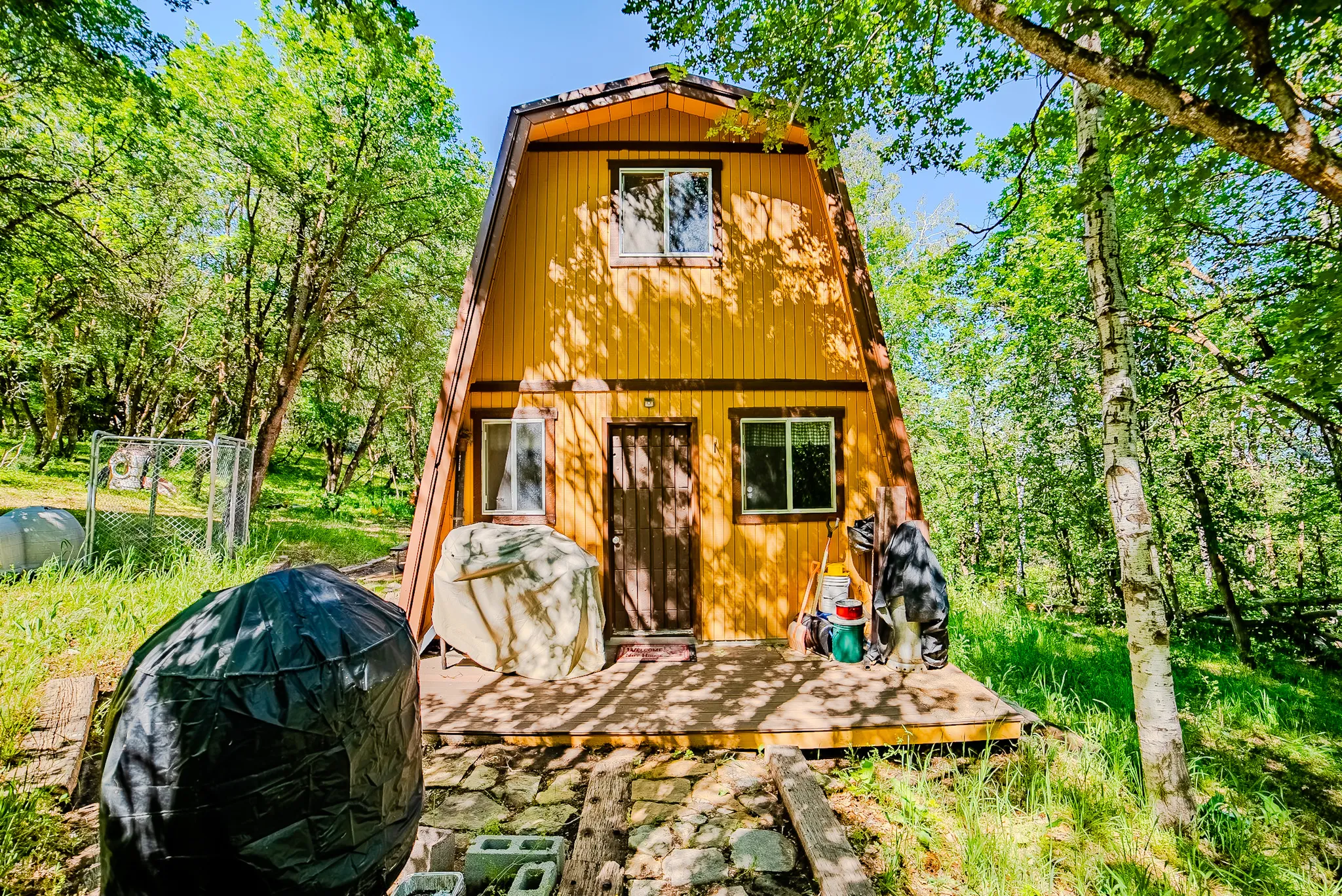 A-frame exterior with yellow siding and dark trim, featuring a ground-level wooden deck