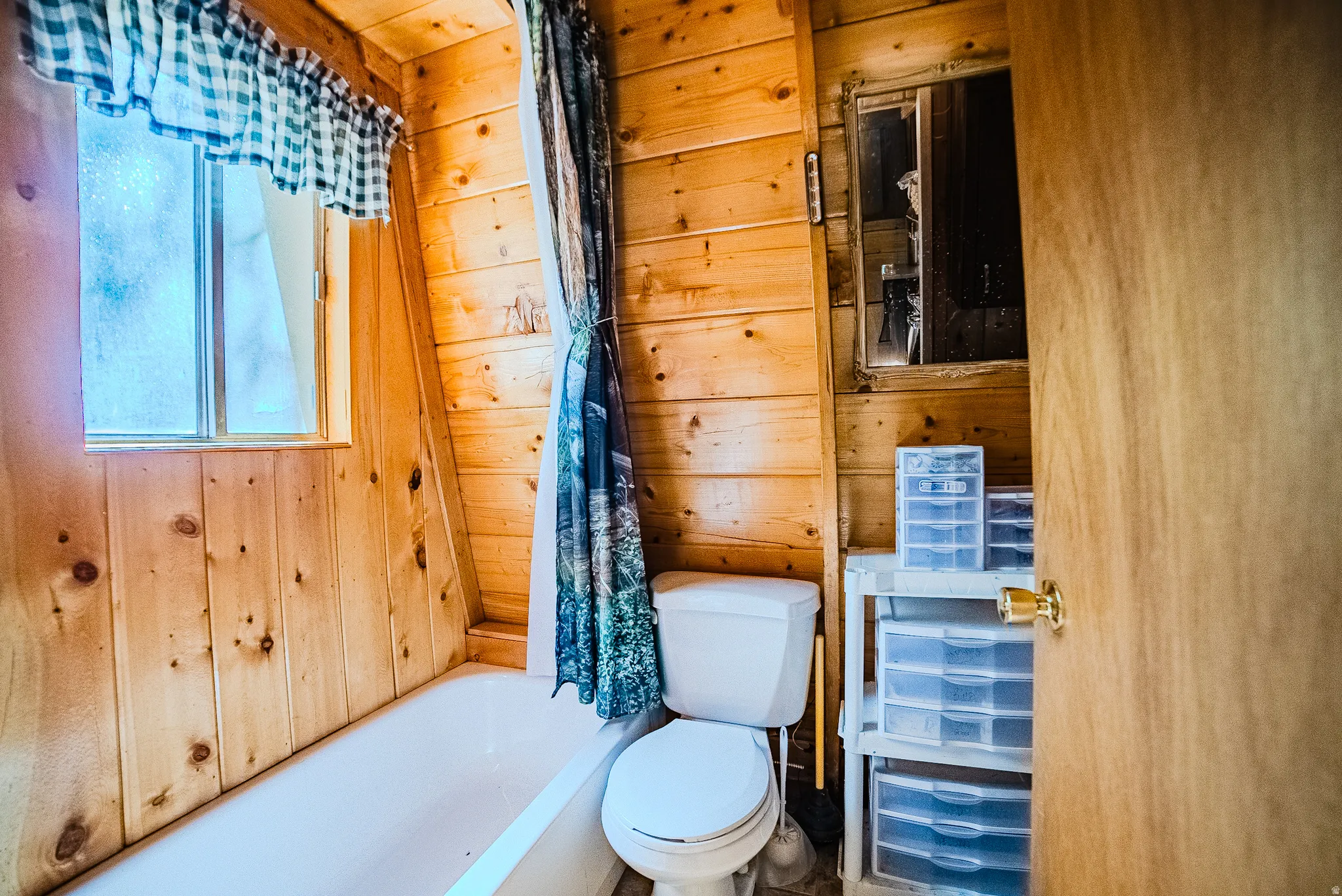 Bathroom featuring light wood-finish paneled walls, a white porcelain bathtub, and a window with a valance