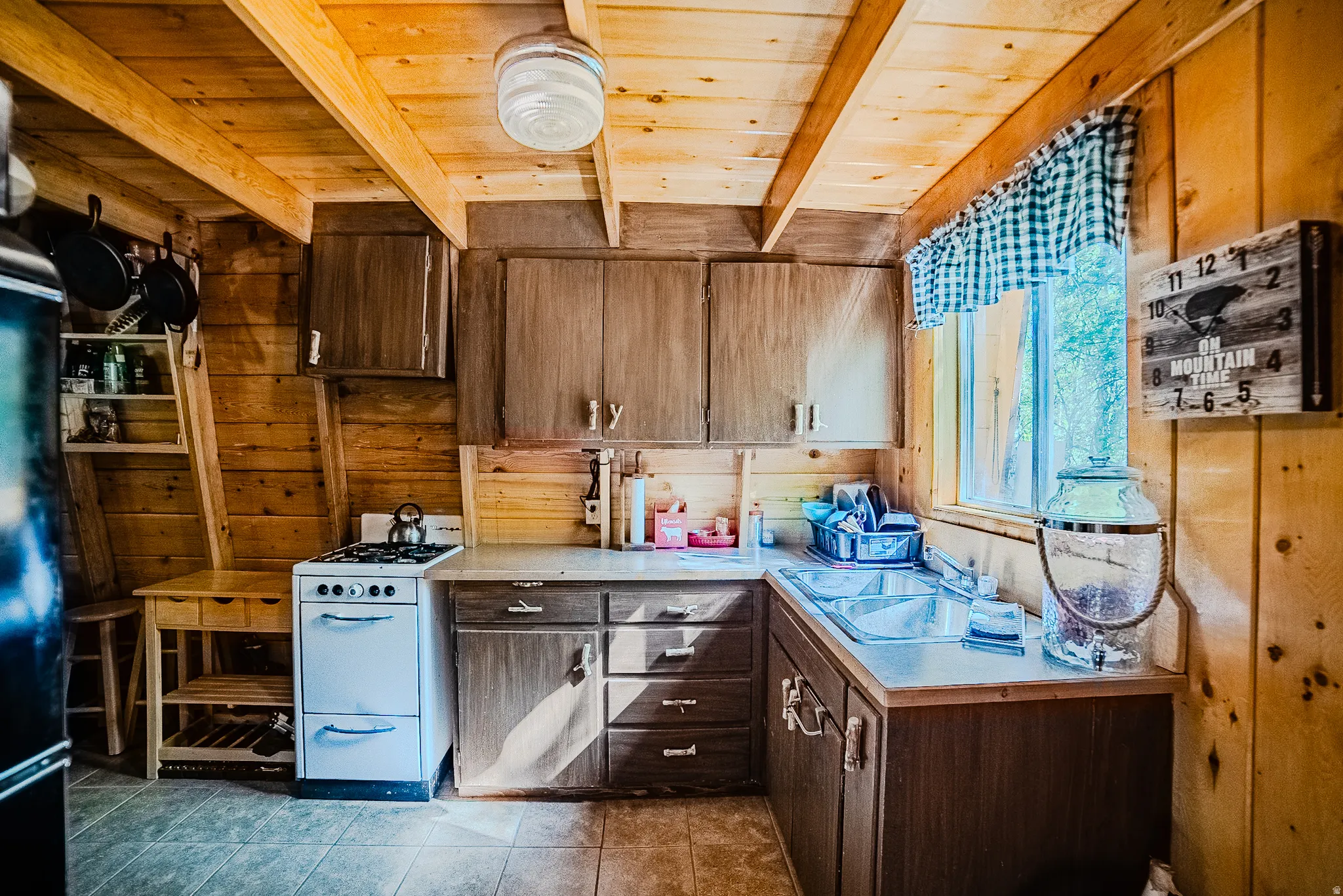 Kitchen featuring wood-paneled walls and ceiling, a double basin stainless steel sink, a window, and built-in cabinetry with wood-finish doors