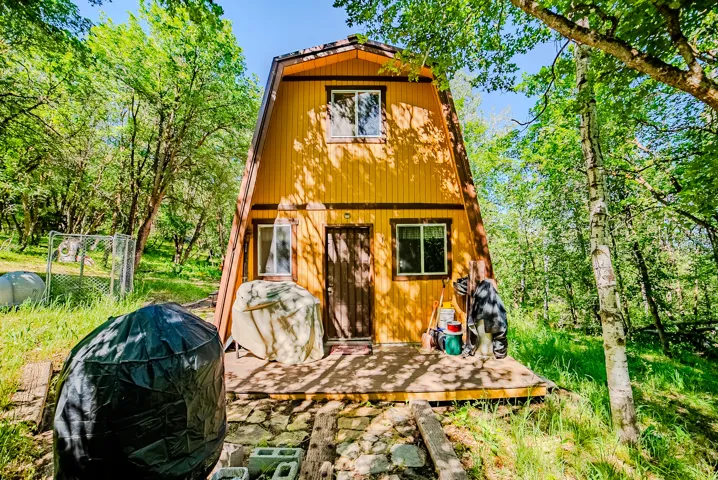 A-frame exterior with yellow siding and dark trim, featuring a ground-level wooden deck