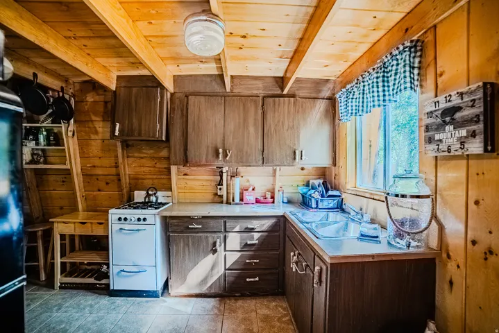 Kitchen featuring wood-paneled walls and ceiling, a double basin stainless steel sink, a window, and built-in cabinetry with wood-finish doors