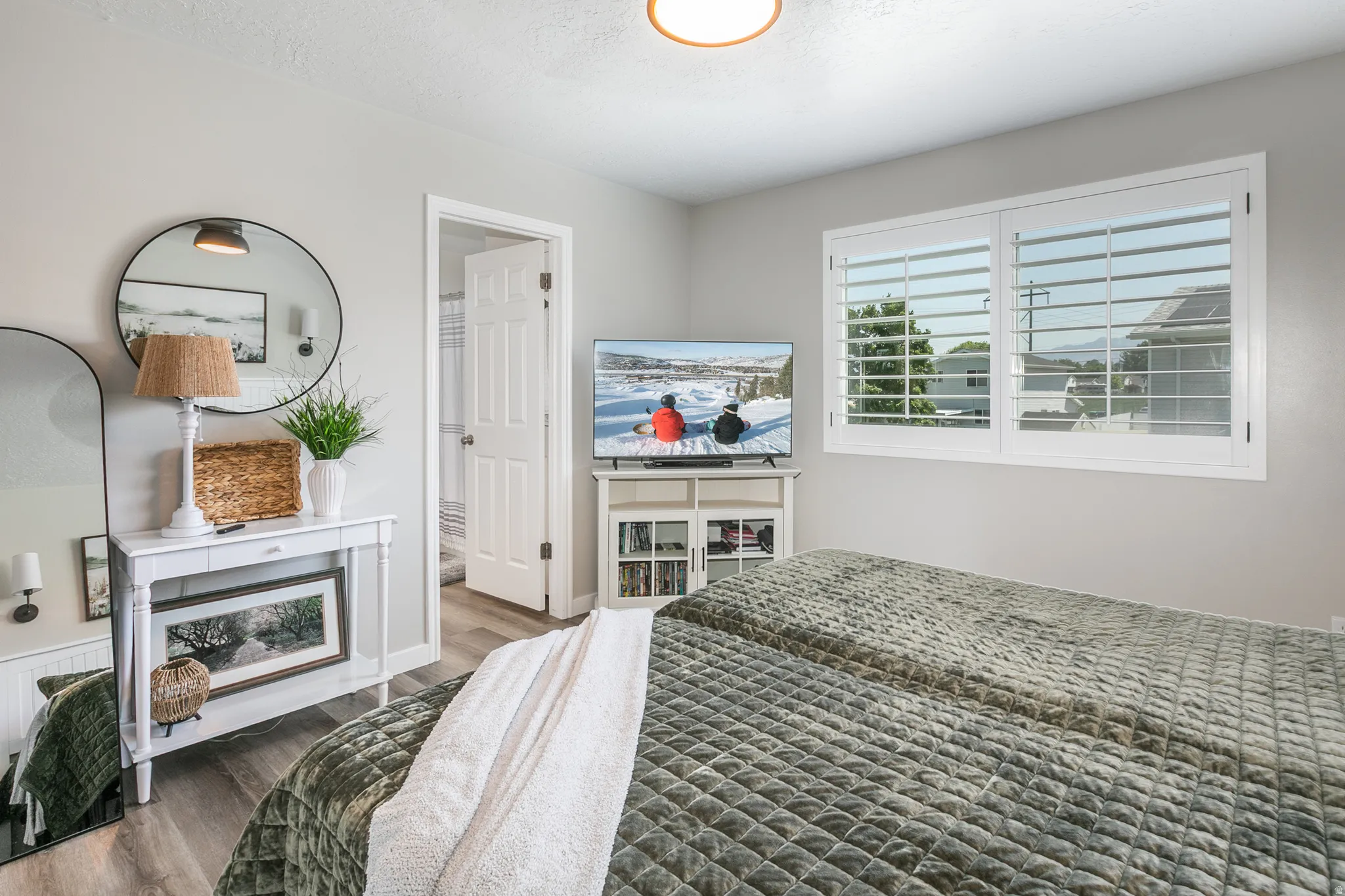Light-filled room featuring wood-finish flooring, a ceiling-mounted light fixture, and a window with white plantation shutters