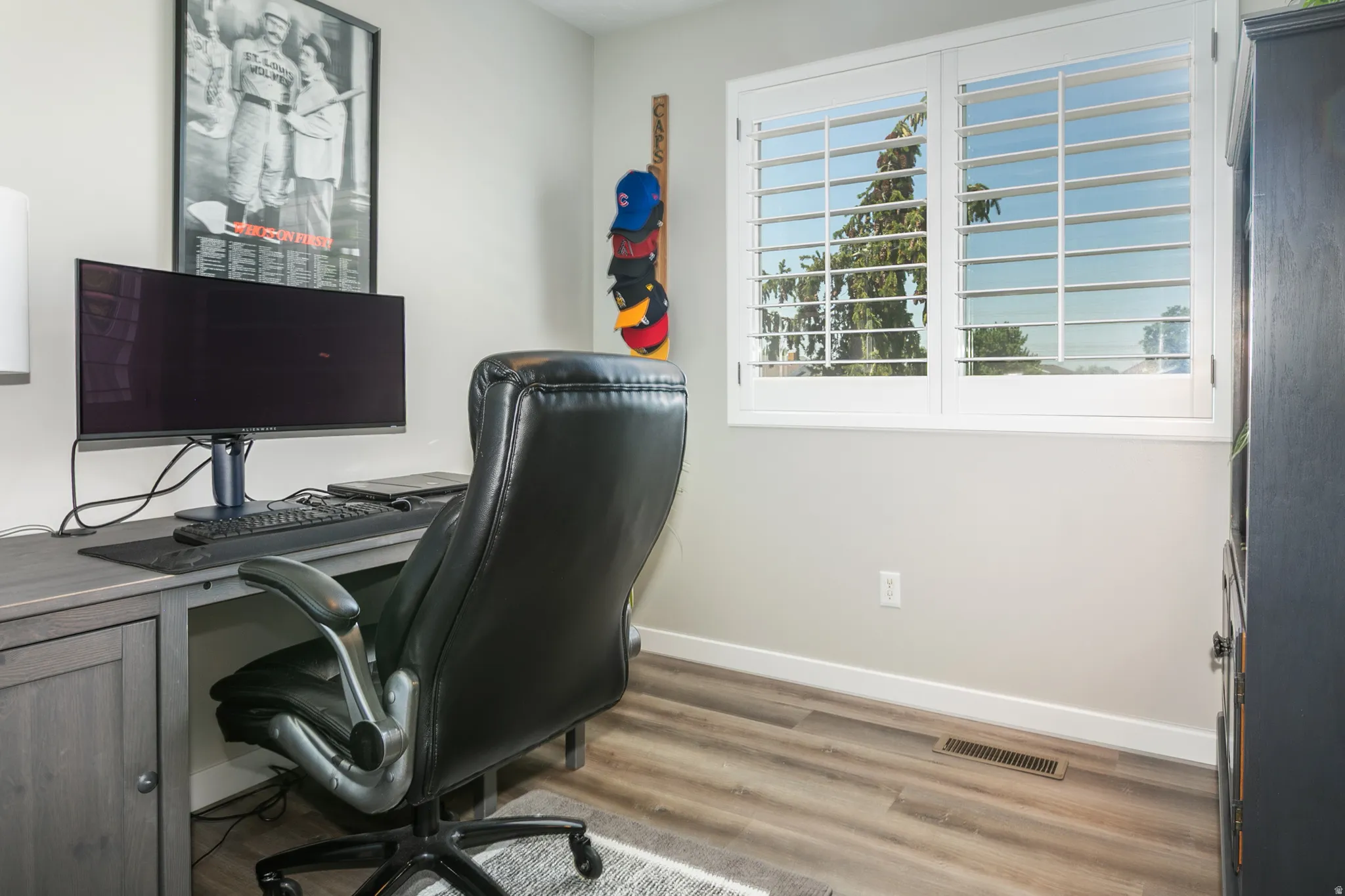 Room featuring wood-finish flooring, white baseboards, and a window with white plantation shutters