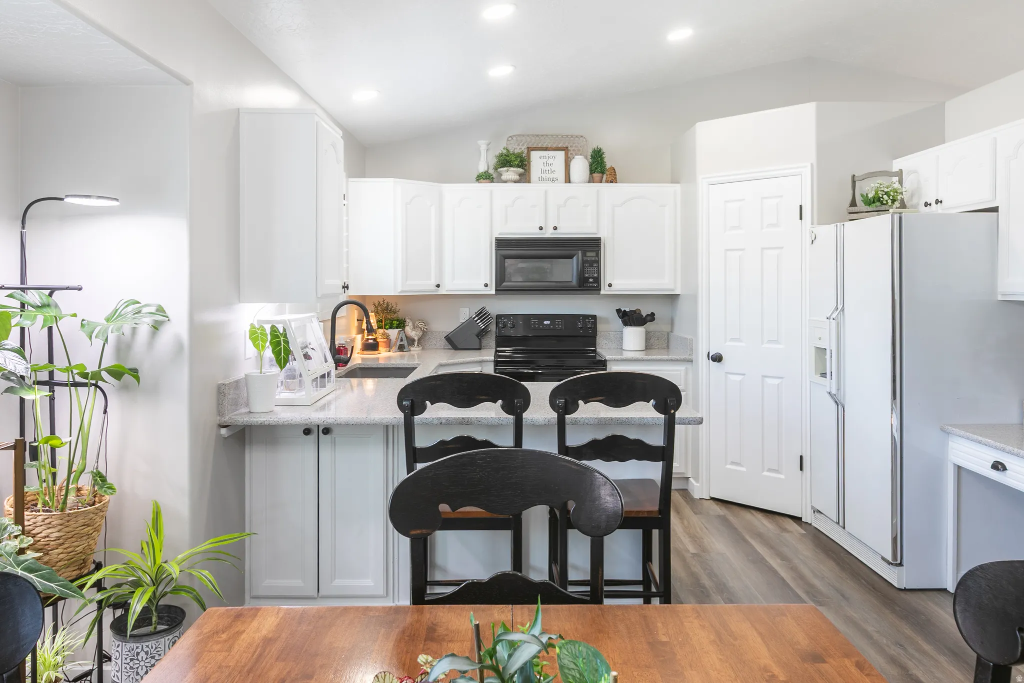 White cabinetry with black hardware, granite-style countertops, stainless steel appliances, wood-finish flooring, and recessed lighting