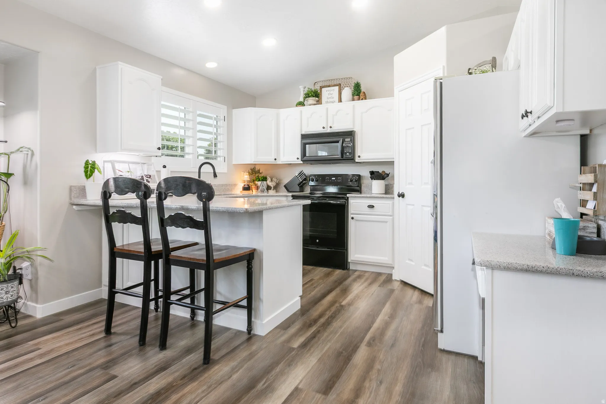 Kitchen featuring wood-finish flooring, white cabinetry, integrated black appliances, and a breakfast bar with stone-finish countertops