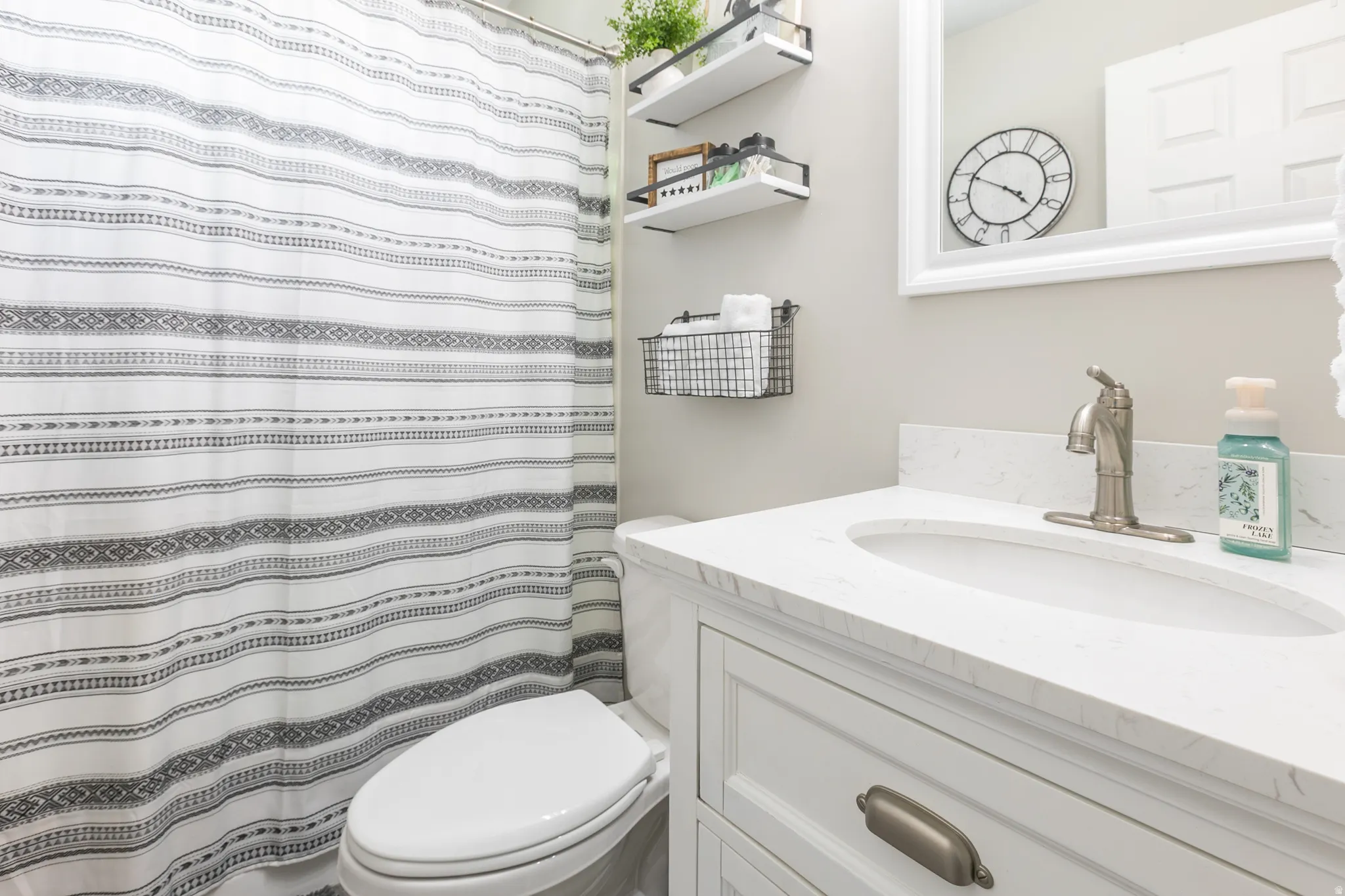 Bathroom featuring a single vanity with a white countertop and undermount sink, brushed nickel faucet, and white cabinet with bronze hardware