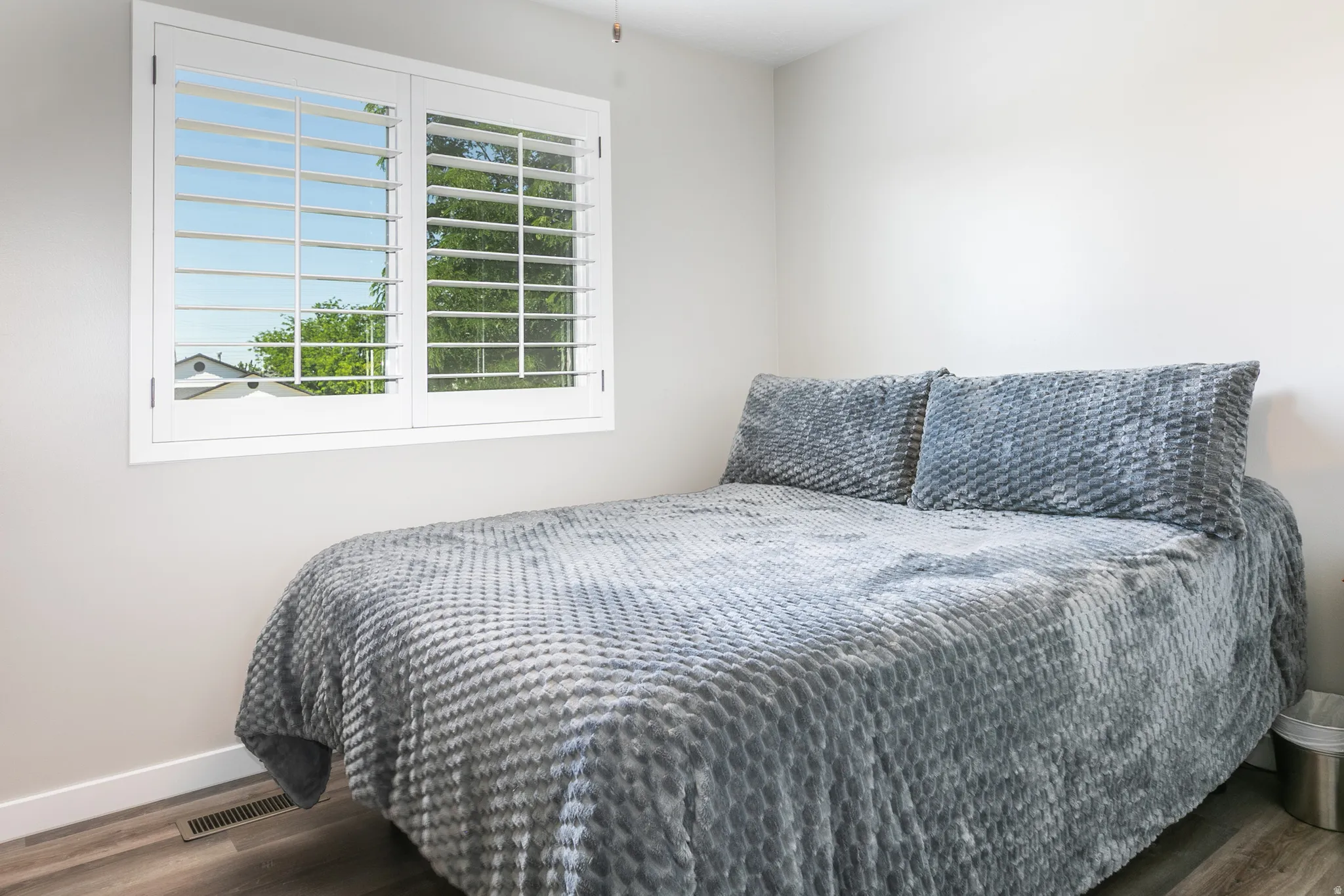 Bright interior room featuring a window with white louvered shutters, light gray walls, and wood-finish flooring