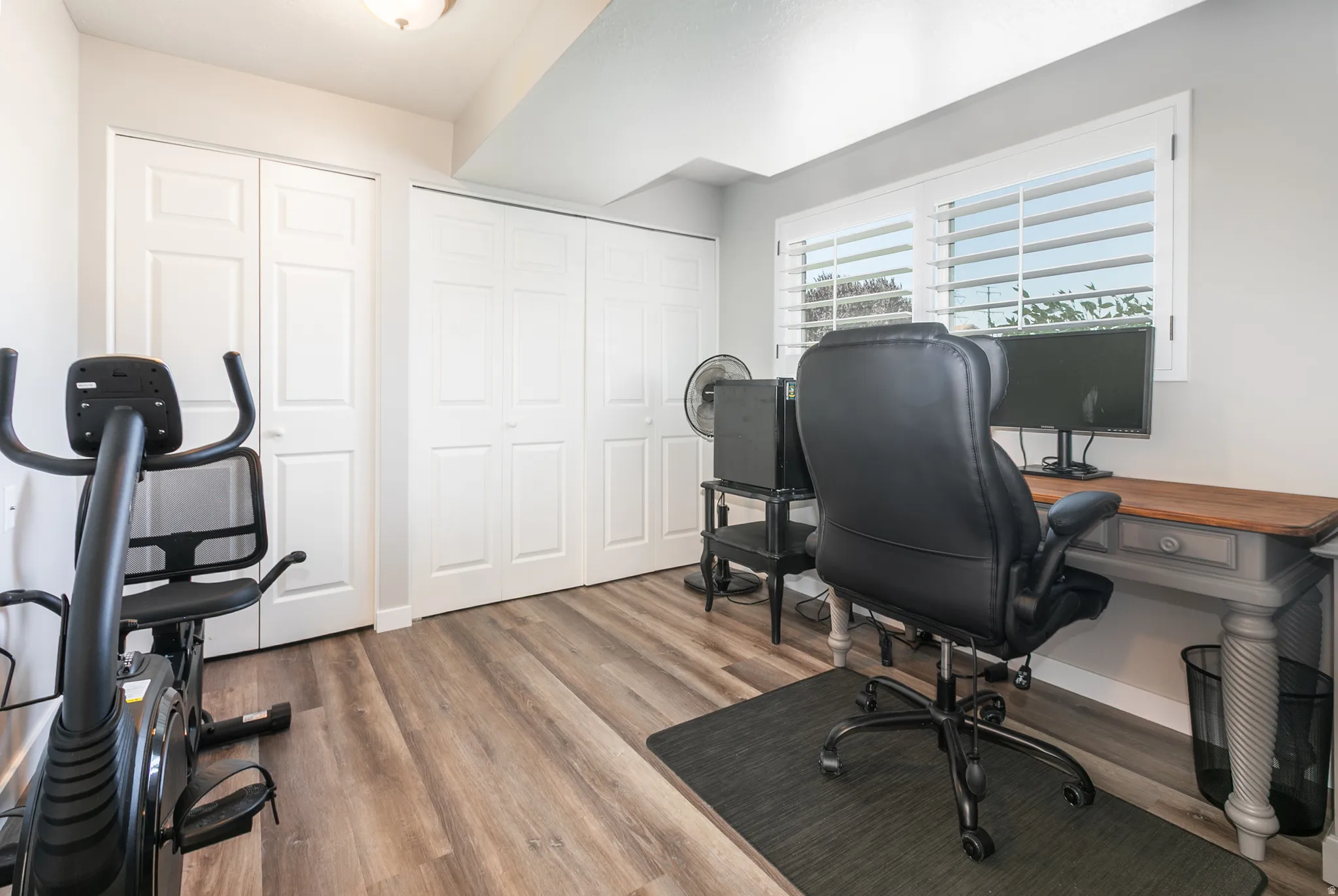 Versatile room featuring wood-finish flooring, white plantation shutters, and multiple paneled closet doors