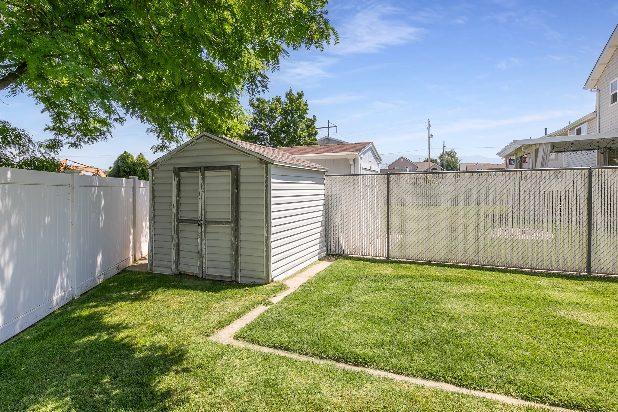 Spacious backyard featuring a storage shed, a white privacy fence, a chain-link fence, and mature trees