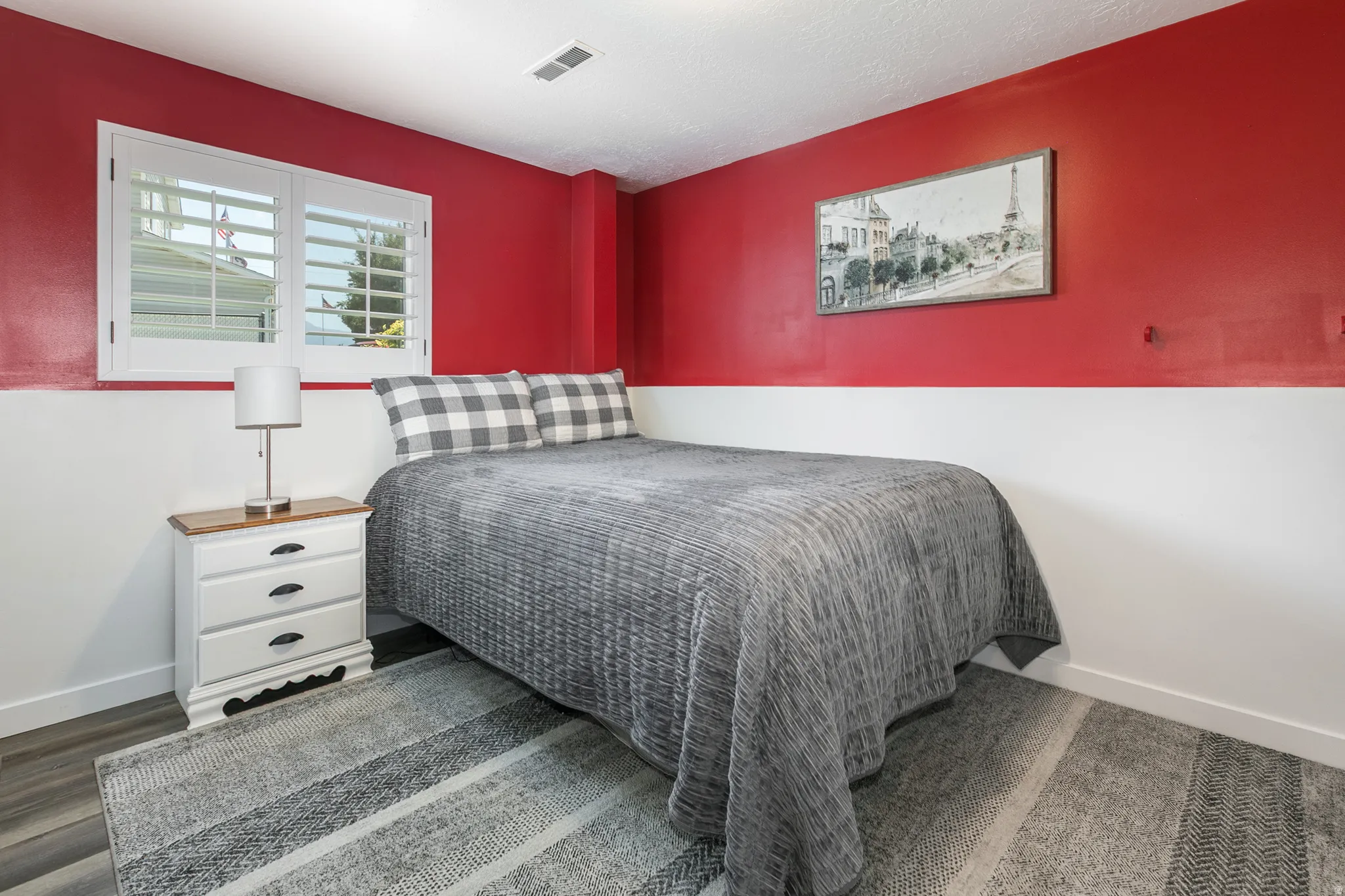 Room featuring a window with white louvered shutters, two-tone walls with a red upper and white lower section, and wood-finish flooring