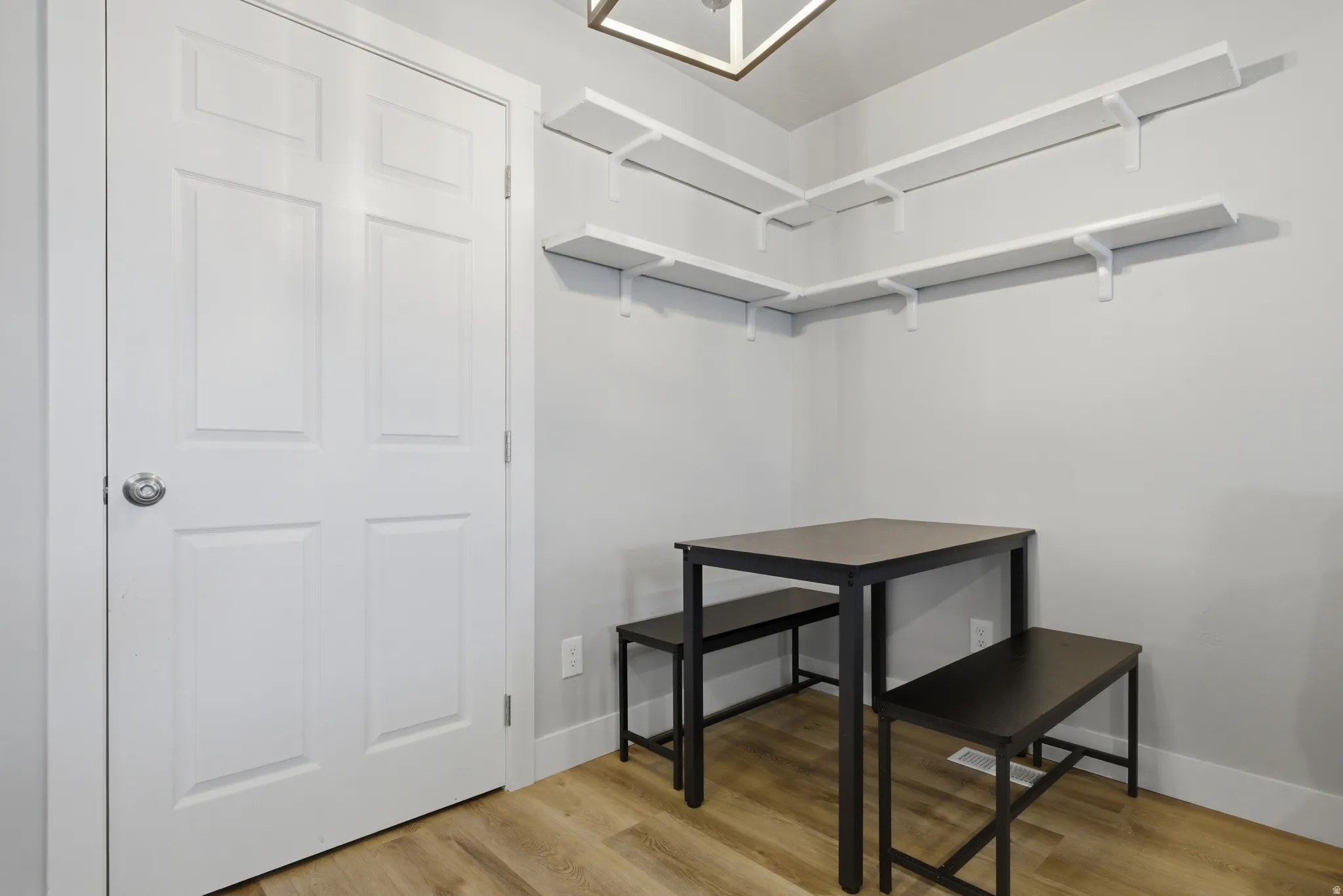 Corner dining area featuring wood-finish flooring, light gray walls, and white floating shelves
