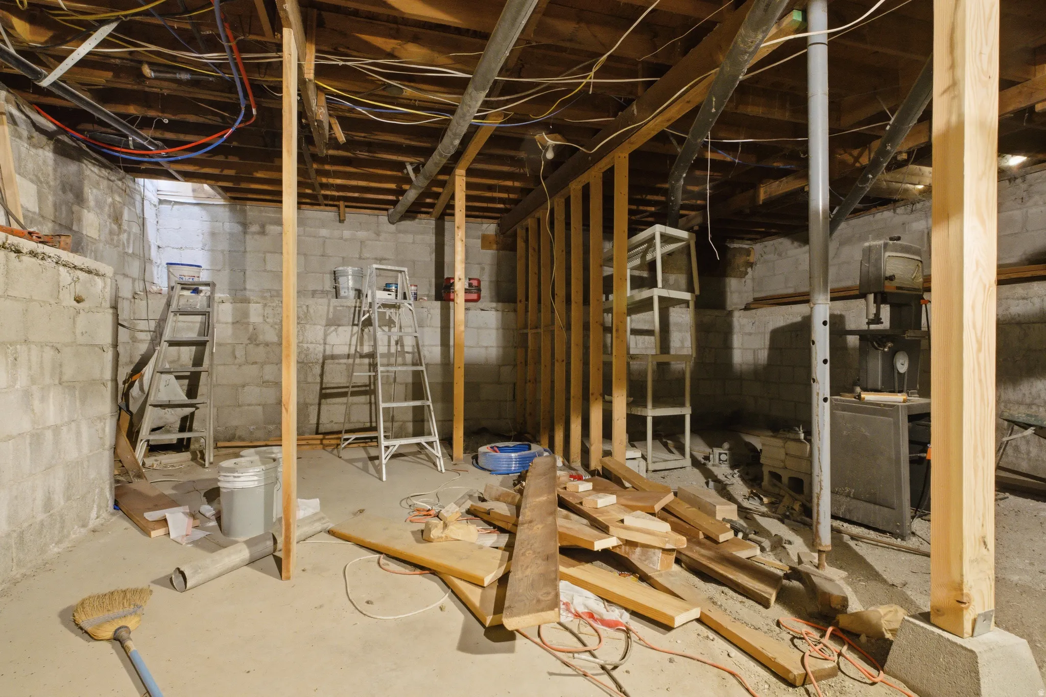 Unfinished basement featuring concrete block walls, exposed wood ceiling joists, and a concrete floor