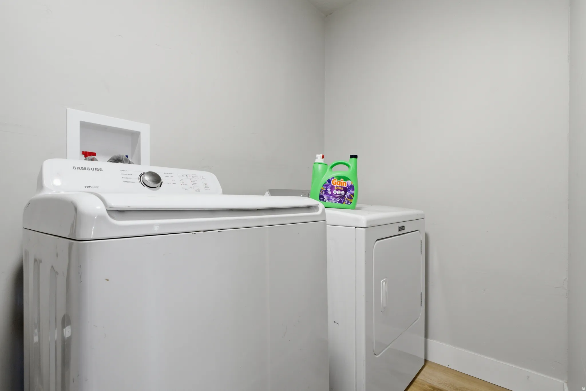 Dedicated laundry area featuring light-toned walls and wood-finish flooring