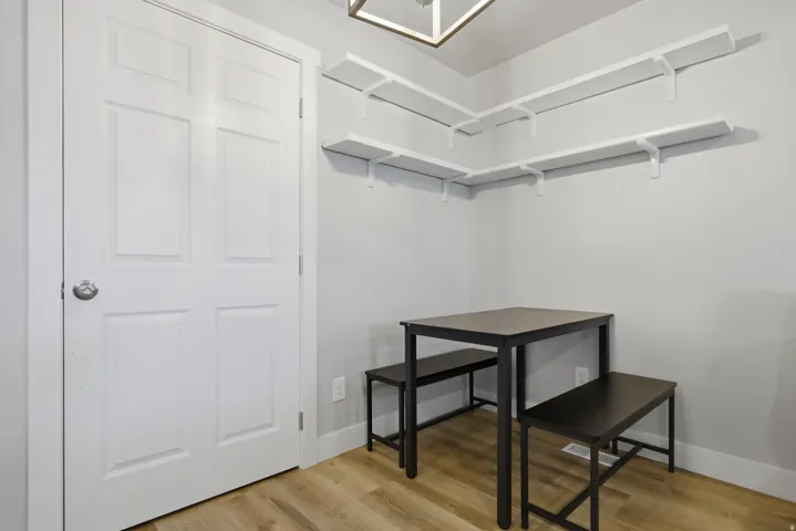 Corner dining area featuring wood-finish flooring, light gray walls, and white floating shelves