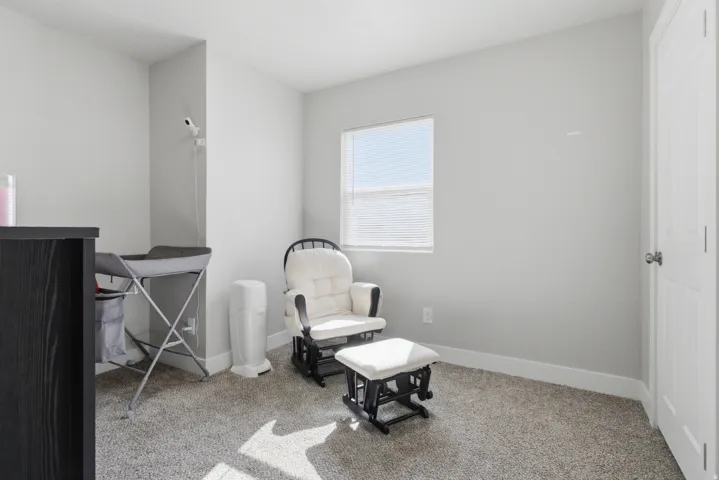 Carpeted room with light gray walls, a single window featuring horizontal blinds, and a white paneled door with a brass-finish knob