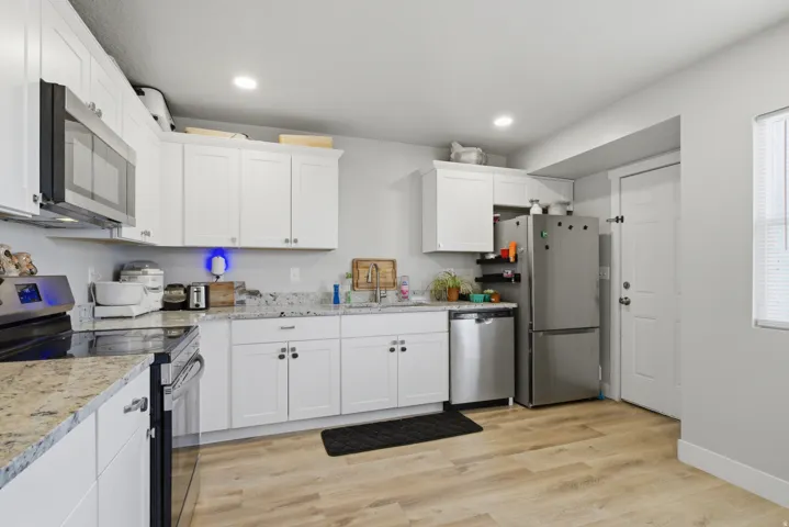 Kitchen featuring white cabinetry, light-colored speckled countertops, stainless steel appliances, recessed lighting, and wood-finish flooring