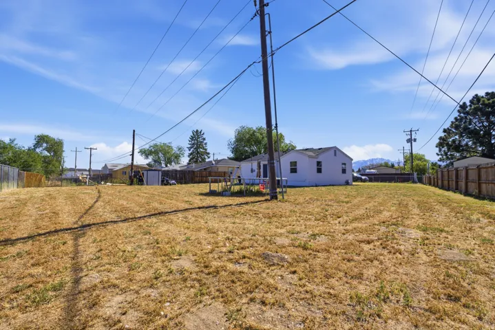Expansive yard space with perimeter fencing, a white single-story residence, and distant mountain scenery under a clear sky