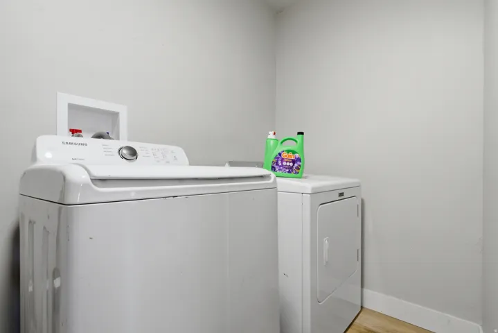 Dedicated laundry area featuring light-toned walls and wood-finish flooring