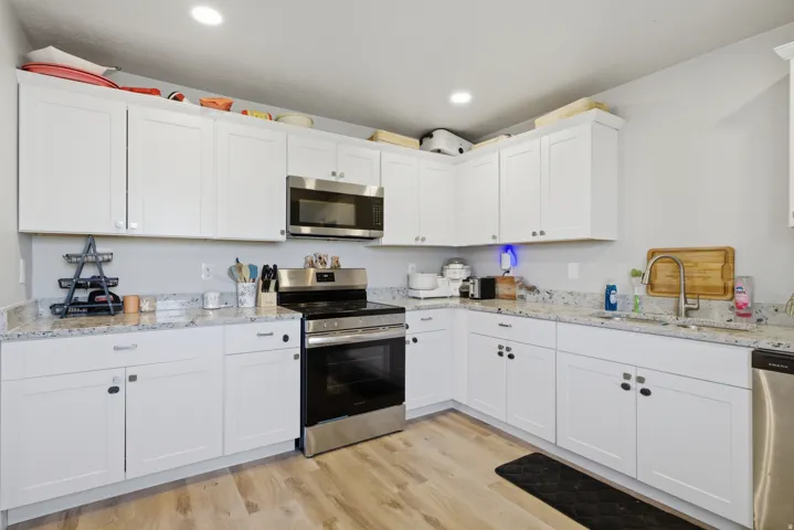 Modern kitchen featuring white shaker cabinetry, speckled countertops, stainless steel appliances, and wood-finish flooring