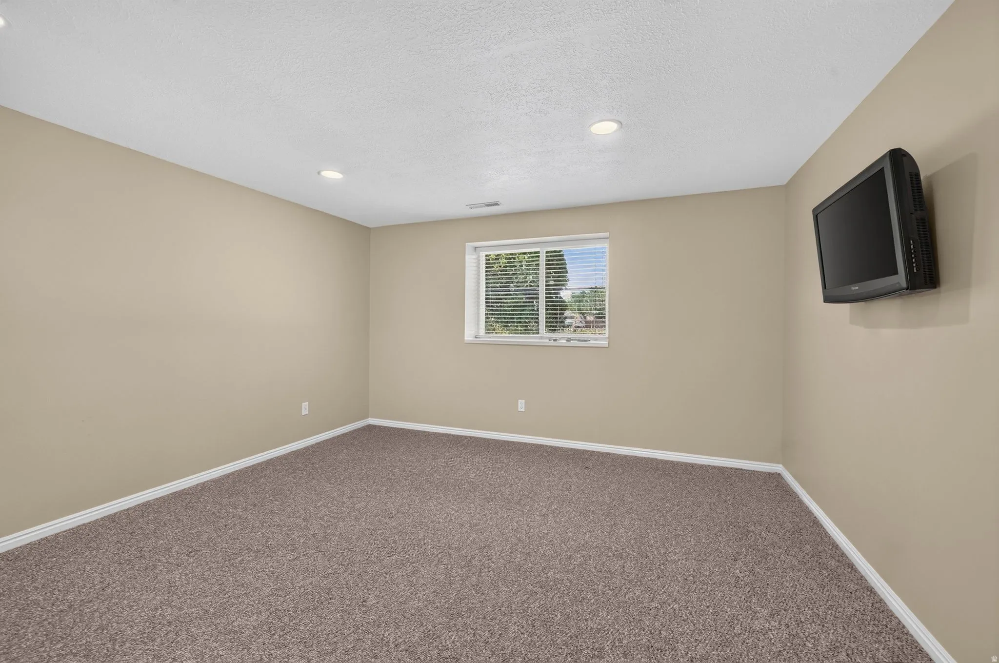 Neutral-toned room featuring recessed lighting, a window with horizontal blinds, and textured carpeting