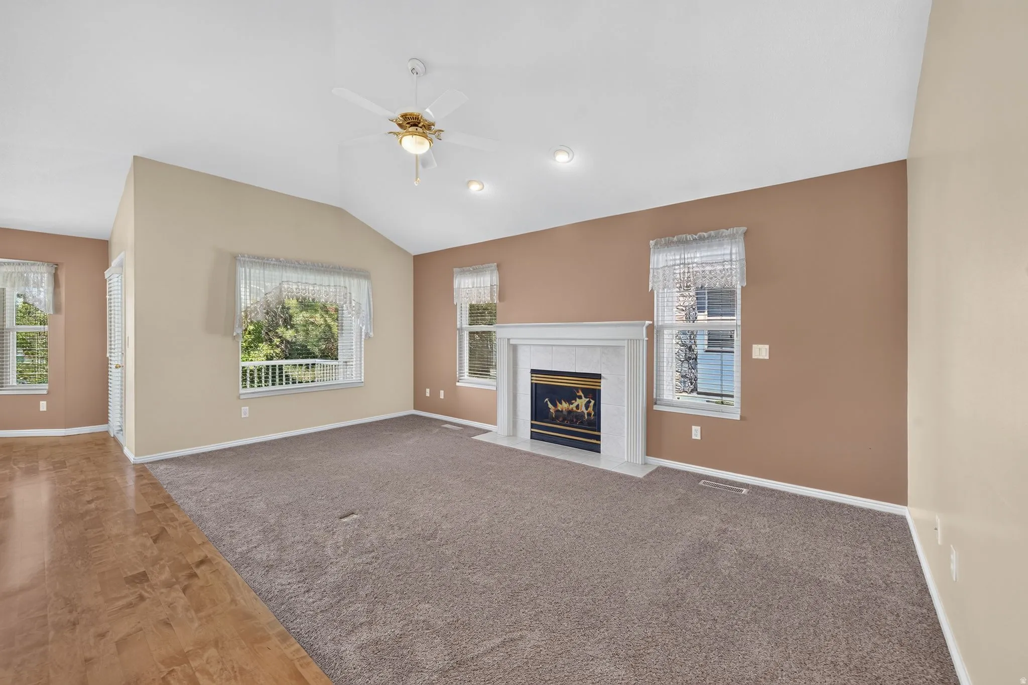 Spacious living area featuring a vaulted ceiling with a ceiling fan, a white mantel fireplace, and recessed lighting