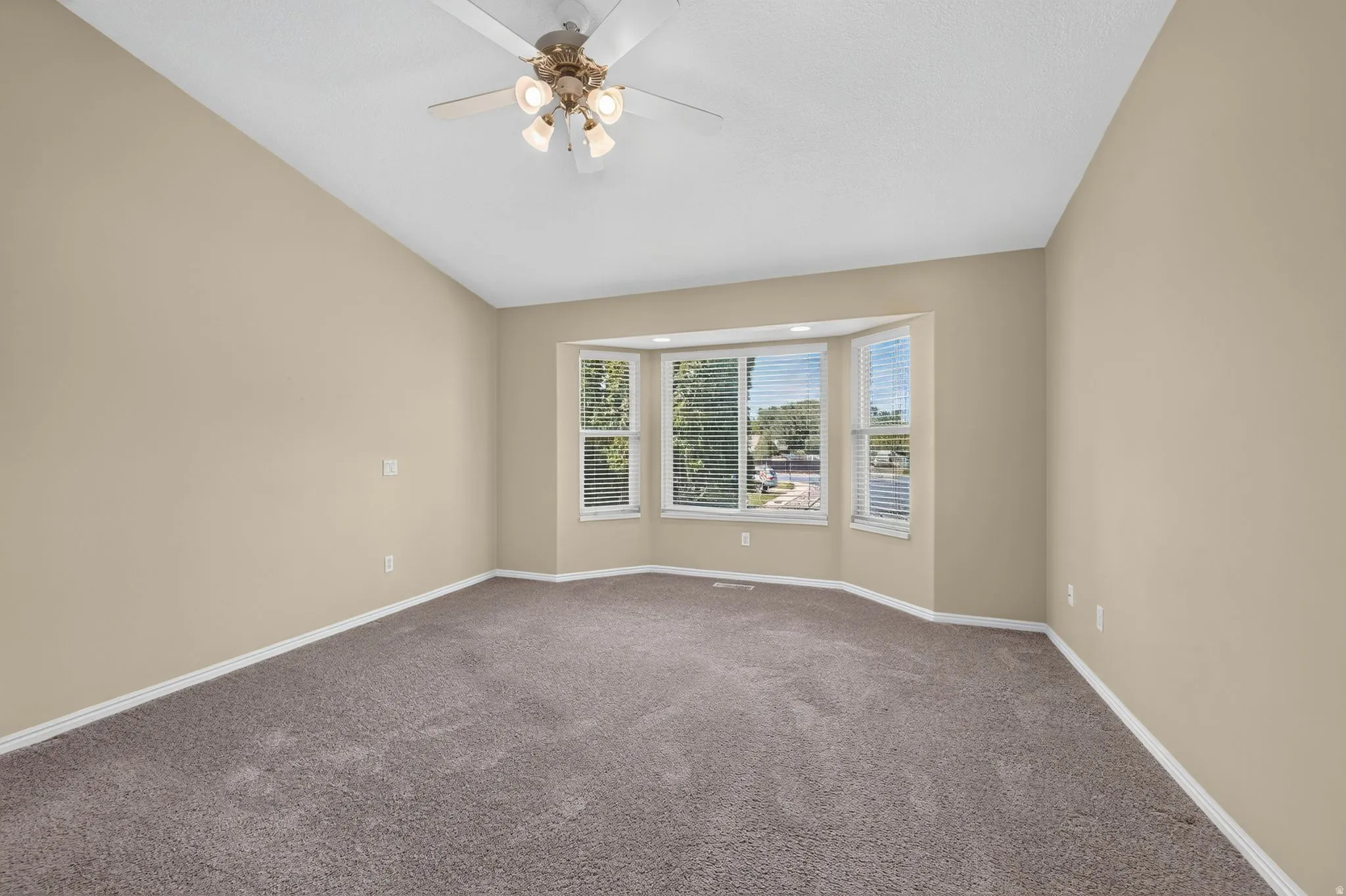 Bay window with horizontal blinds, sloped ceiling, overhead ceiling fan with integrated lighting, neutral-toned walls, and carpet flooring