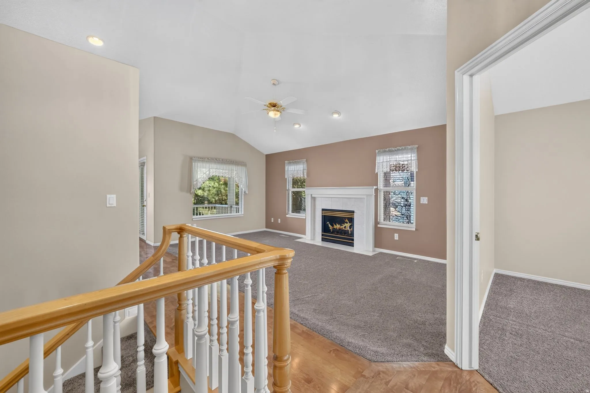 Living area featuring a vaulted ceiling with recessed lighting and a ceiling fan, a white mantel fireplace, and multiple windows