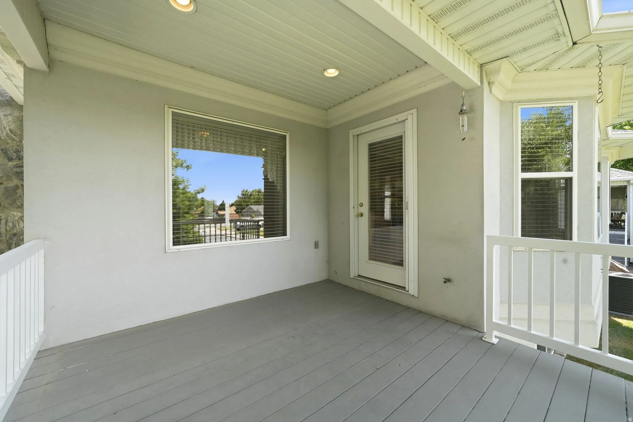 Covered outdoor deck with painted wood-finish flooring, white railing, and recessed lighting