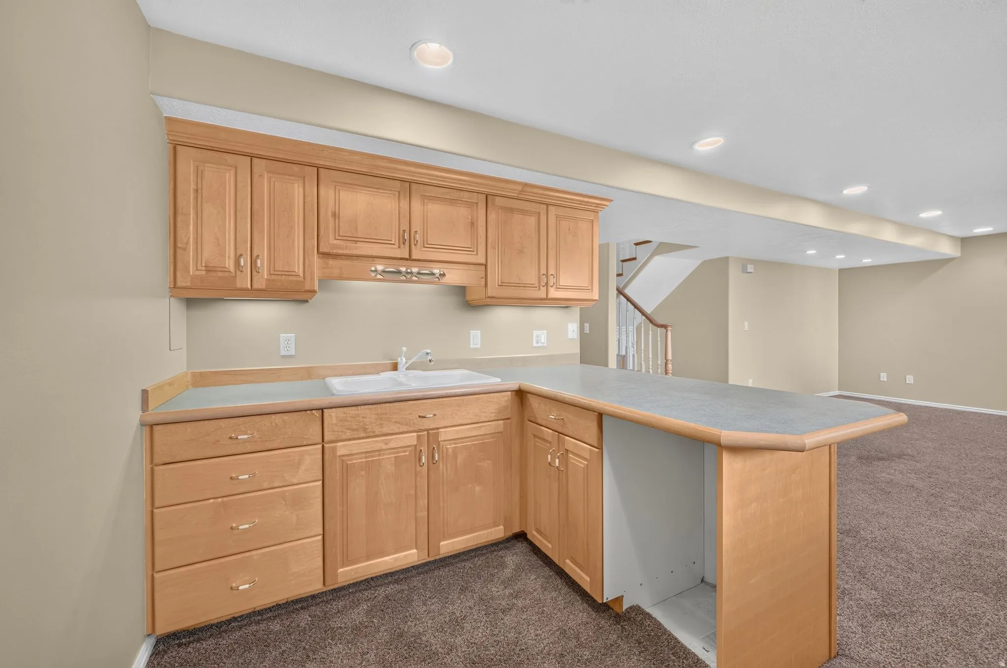Wet bar featuring light wood cabinetry, a double basin sink, light-toned countertop, and recessed lighting