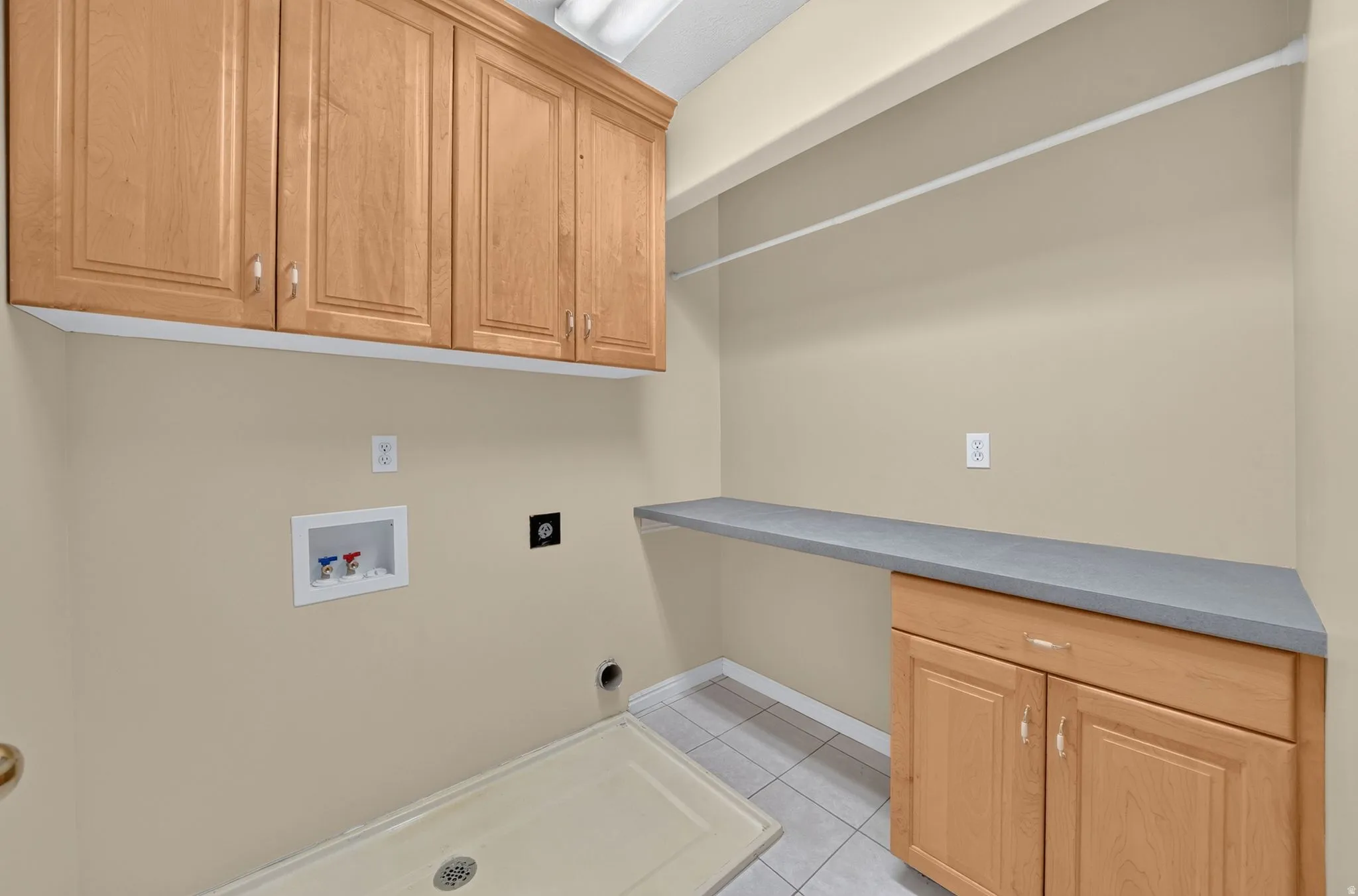Laundry area featuring light wood cabinetry, a utility sink, a built-in countertop, and tile flooring