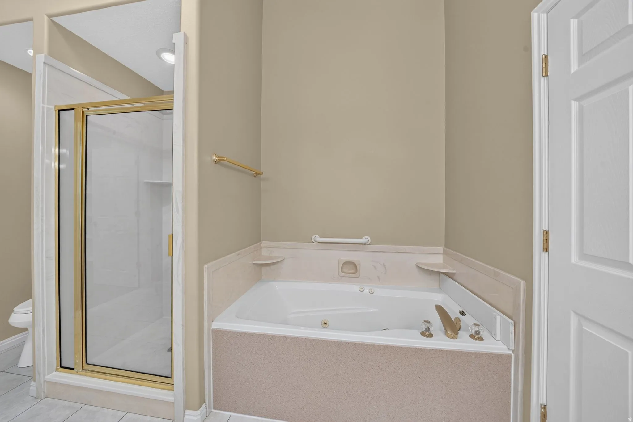 Bathroom featuring a built-in jetted tub with gold-toned fixtures, a framed glass shower enclosure, beige wall paint, a white paneled door, and recessed lighting