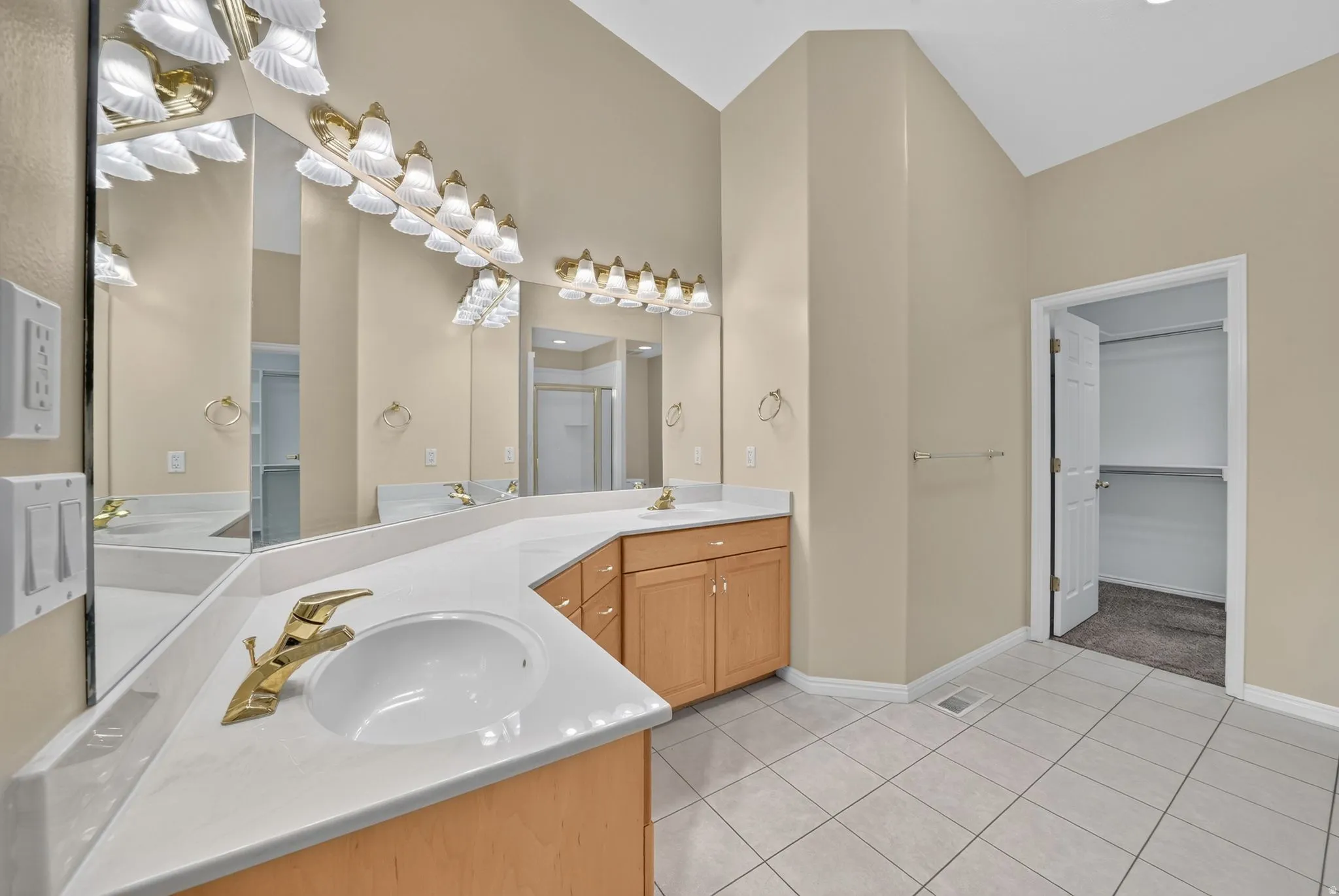 Bathroom featuring a dual vanity with light-tone wood cabinetry, white countertops, and gold-finish fixtures