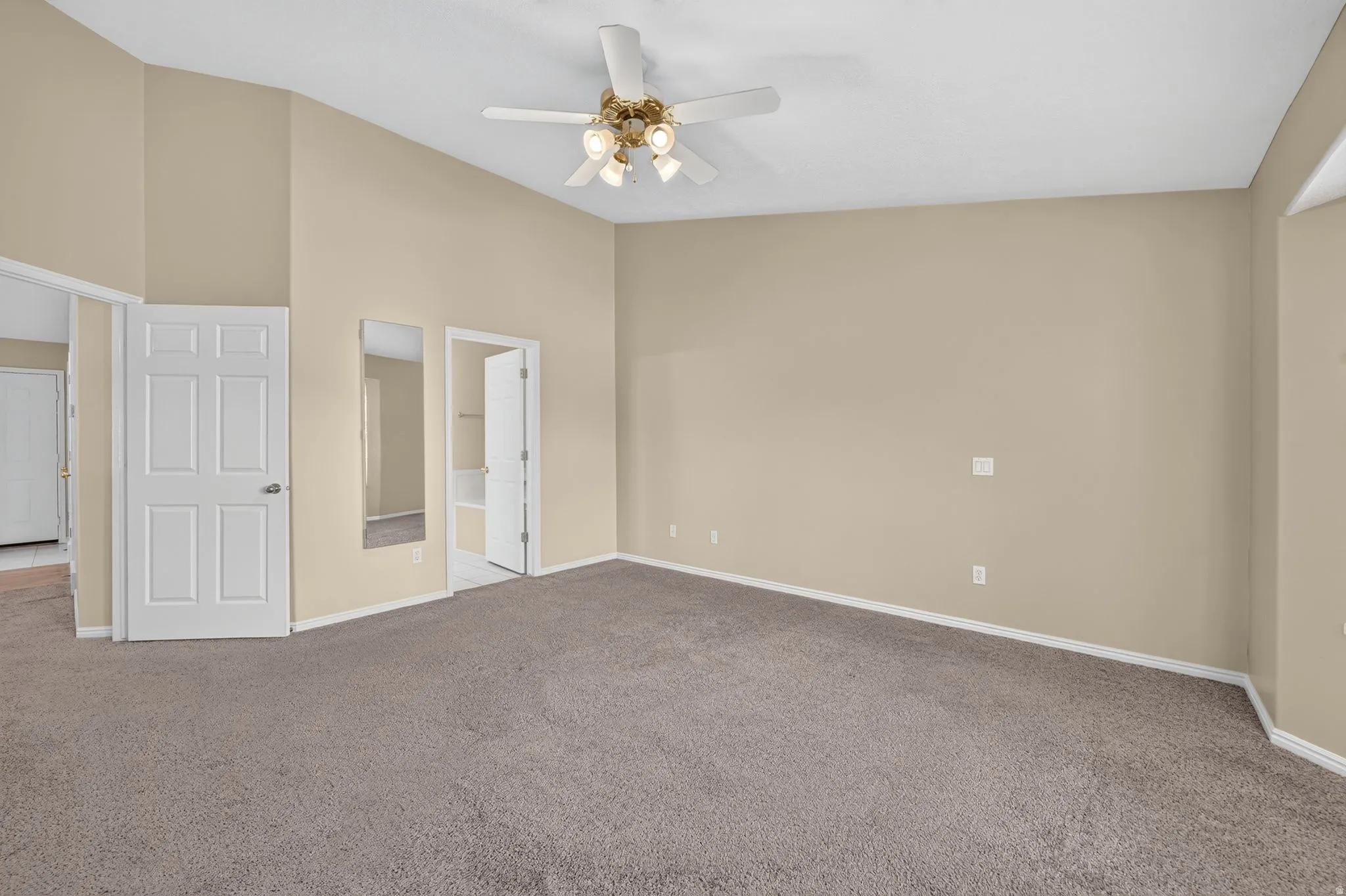 Spacious room featuring vaulted ceilings, a ceiling fan with integrated lighting, neutral-toned walls, and plush carpet flooring
