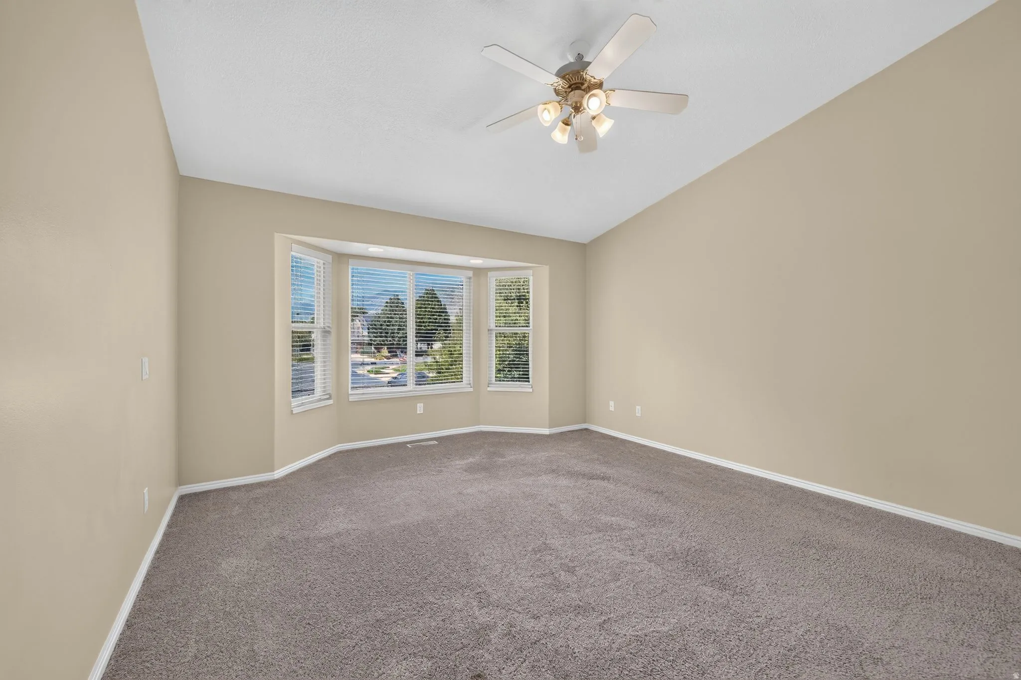 Spacious room featuring a bay window with blinds, vaulted ceiling, and a ceiling fan with integrated lighting