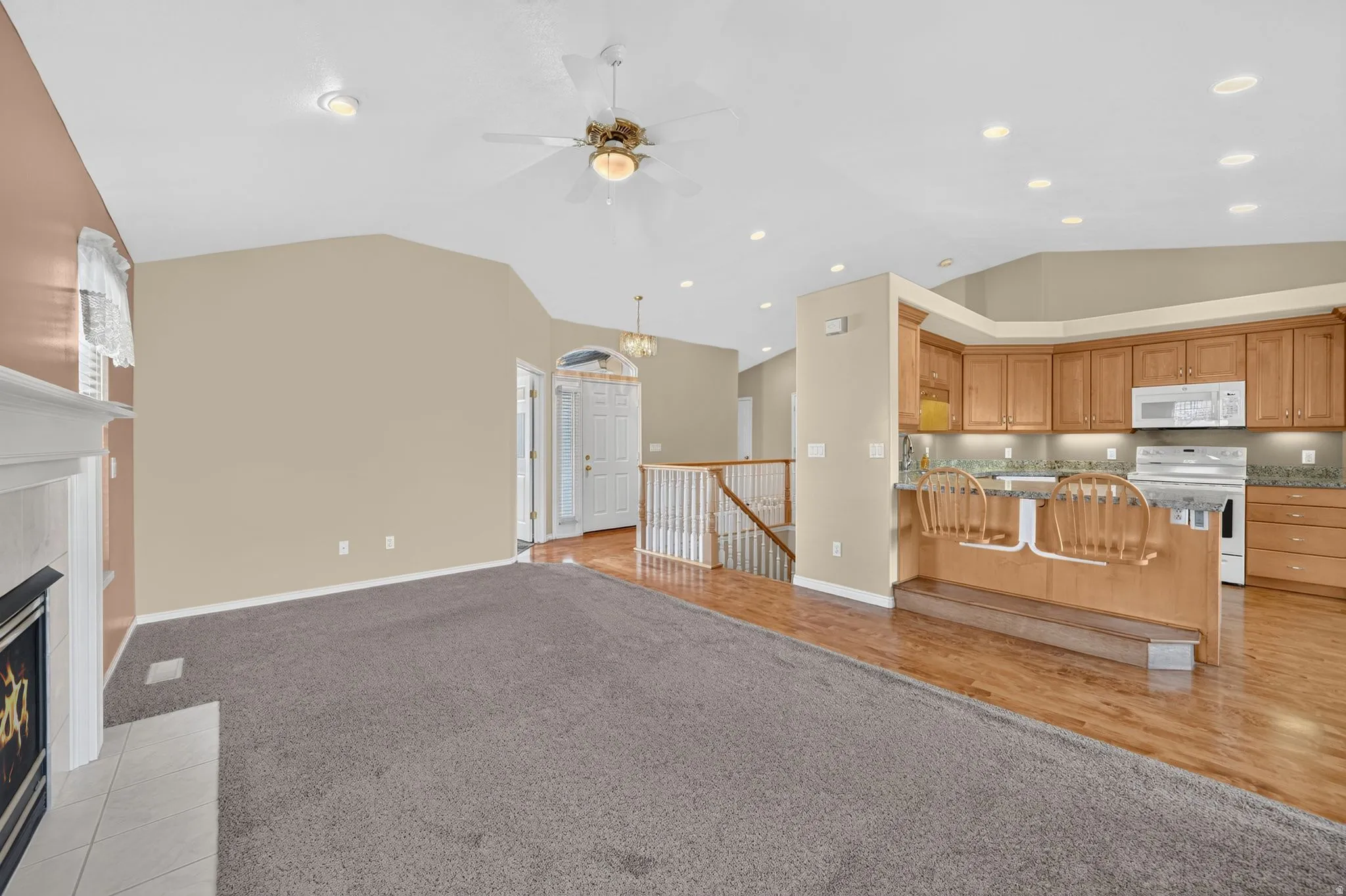 Open-concept living area featuring vaulted ceilings, a fireplace with a white mantle, wood-finish flooring, a kitchen with wood cabinetry and stainless steel appliances, and recessed lighting